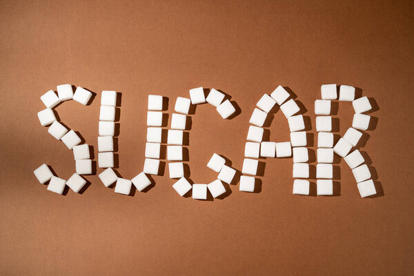 Слово сахар из сахара белые кубики на коричневом фоне