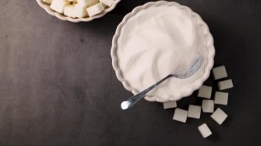 Bir kasede beyaz şeker küpleri ve granüller. Koyu arkaplan.