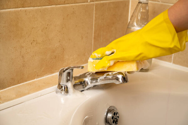 Cleaning bathroom water tap, yellow gloves and spray cleaning product.