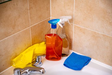 Sprey deterjan, banyo tüpü ve su musluğu, sarı eldivenler ve bez..