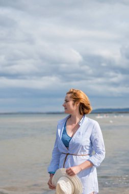 Deniz kenarında güneş şapkalı bir kadın, tatilinin tadını çıkarıyor. Bulutlu bir gün