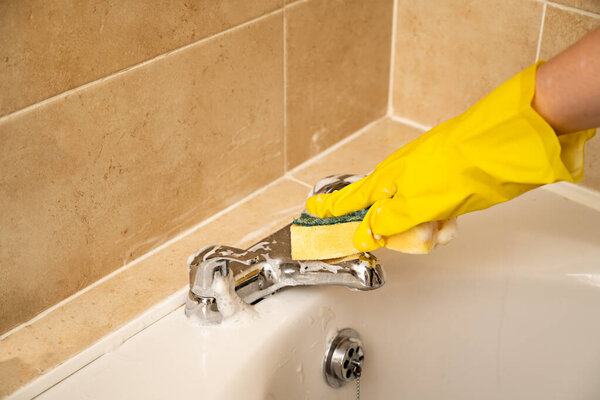 Cleaning bathroom water tap, yellow gloves and spray cleaning product.