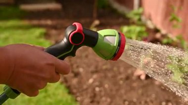 Bahçeyi sulayan hortumlu ve su jetli bir erkek..