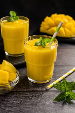 Taze meyve ve nane arkaplanlı bir bardakta mango muzlu smoothie.