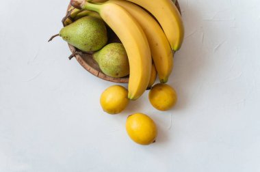 Masadaki ahşap tabakta olgun muz, armut ve limon. İzole edilmiş beyaz arka plan. Sağlıklı tropikal yiyecekler.