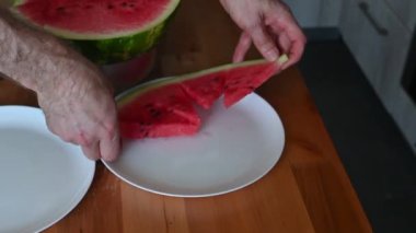 Ahşap bir masada taze karpuz dilimleyip servis eden eller meyvelerin canlı rengini renklendiriyor.