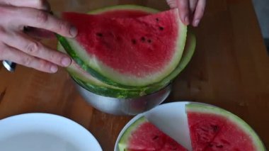 Ahşap bir masada taze karpuz dilimleyip servis eden eller meyvelerin canlı rengini renklendiriyor.