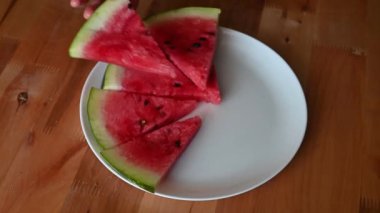 Ahşap bir masada taze karpuz dilimleyip servis eden eller meyvelerin canlı rengini renklendiriyor.