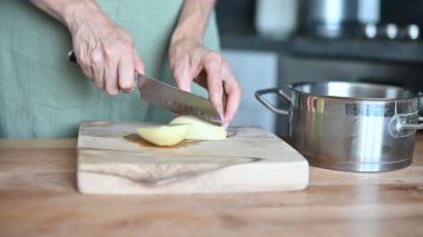 Patates dilimliyorum. Sebze doğrayan bir bıçağın yakın çekimi. Yemek pişirmek. Bir kadın, taze patatesleri, evde yemek hazırlama işlemini ahşap bir mutfak tahtasıyla keser..