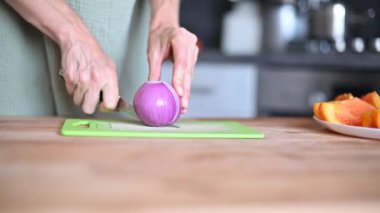 Bıçak, mutfak tahtasının üzerinde pembe soğan keser. Kadın soğanı parmaklarıyla kesiyor, sebze kesiyor kadın yemek pişiriyor.