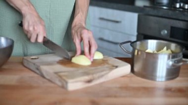 Patates dilimliyorum. Sebze doğrayan bir bıçağın yakın çekimi. Yemek pişirmek. Bir kadın, taze patatesleri, evde yemek hazırlama işlemini ahşap bir mutfak tahtasıyla keser..