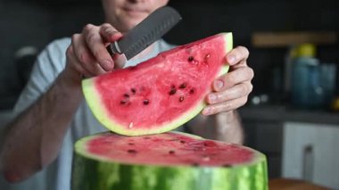 Adamın biri karpuzu ev mutfağında bıçakla parçalara ayırıyor. Ferahlatıcı bir yaz tatlısı.