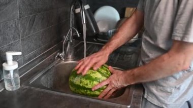 Adam karpuzu mutfakta lavaboda yıkıyor. Kapalı eller organik sebzeleri yıkıyor, yemek hazırlıyor..