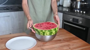 Kadın, ev mutfağında bir karpuzu bıçakla parçalara ayırıyor. Ferahlatıcı bir yaz tatlısı.