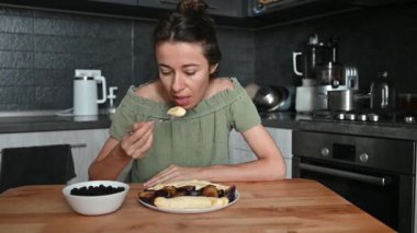 Evde meyve yiyen bir kadın. Mutfaktaki kadın portresi vejetaryen yemekleri ve organik sağlıklı yemekleri sever..