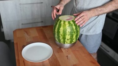 Adamın biri karpuzu ev mutfağında bıçakla parçalara ayırıyor. Ferahlatıcı bir yaz tatlısı.