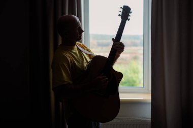 Gitaristin silueti pencereye karşı akustik gitar ödüyor. Stüdyoda müzik enstrümanında müzisyen.