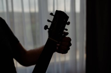 Gitaristin silueti pencereye karşı akustik gitar ödüyor. Stüdyoda müzik enstrümanında müzisyen.