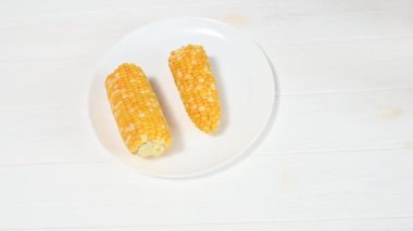 Kadın seramik tabağa mısır koçanı koyuyor. Ev mutfağında vejetaryen yemeği pişirmek. Üst görünüm.