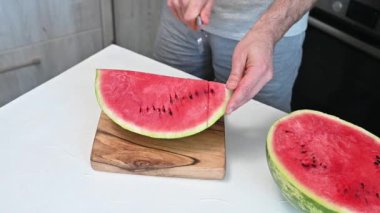 Adamın biri karpuzu ev mutfağında bıçakla parçalara ayırıyor. Ferahlatıcı bir yaz tatlısı.