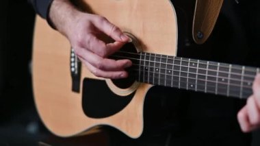 Müzisyen elleri gitar tellerine basar, ahşap akustik enstrümandaki tutkulu performans sırasında melodik ses üretir.