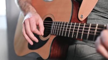 Müzisyen elleri gitar tellerine basar, ahşap akustik enstrümandaki tutkulu performans sırasında melodik ses üretir.