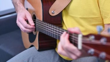 Müzisyen elleri gitar tellerine basar, ahşap akustik enstrümandaki tutkulu performans sırasında melodik ses üretir.