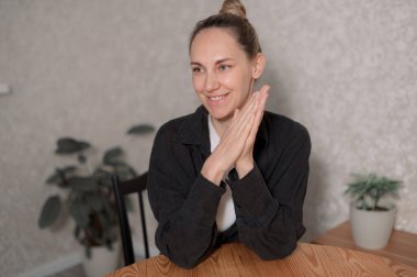 Genç bir kadın, gri bir kanepede rahat rahat oturarak evde vakit geçirmekten zevk alıyor. Gülümsüyor ve rahat görünüyor. Sıcak bir atmosferde yumuşak, doğal bir ışıkla çevrili..