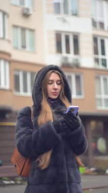Lüks kürklü ve deri eldivenli şık bir kadın. Açık havada cep telefonu kullanıyor. Bağlantının tadını çıkarıyor.
