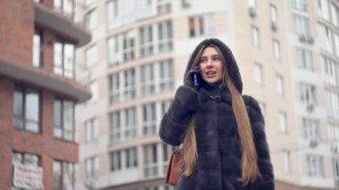 Lüks kürklü ve deri eldivenli şık bir kadın. Açık havada cep telefonu kullanıyor. Bağlantının tadını çıkarıyor.