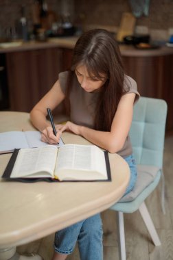 Bayan öğrenci çalışıyor ve evdeki sınava hazırlanıyor. Ders kitabını karıştıran ve notlar alan bir kadın.