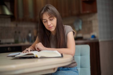 Bayan öğrenci çalışıyor ve evdeki sınava hazırlanıyor. Ders kitabını karıştıran ve notlar alan bir kadın.