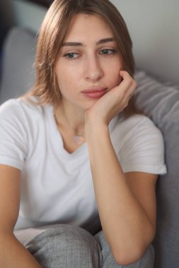 Kafasını tutan genç bir kadın, sinirli, modern oturma odasında kanepede oturuyor..