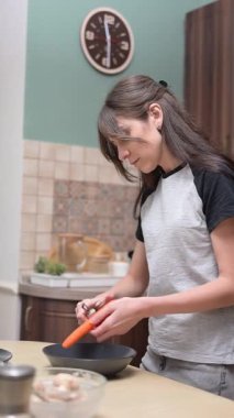 Kadın seramik kasede taze havuç soyuyor, mutfak ortamında besleyici malzemeler hazırlıyor.