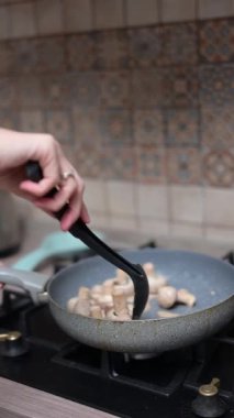 Profesyonel şef, mantarları metal spatulayla karıştırıyor. Çağdaş mutfak çalışma alanında gaz menzilinde lezzetli yemekler pişiriyor.