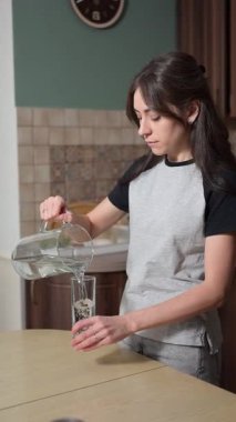 Genç bir kadın mutfakta bir bardak temiz su içiyor. Sağlıklı yaşam tarzı ve hidrasyon konsepti.