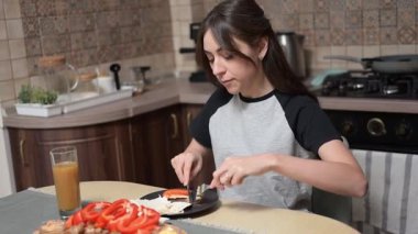 Mutfak masasında oturan genç bir kadın taze sebzeler, pide ekmeği ve besleyici sabah yemeği için meyve suyu hazırlıyor.