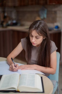 Bayan öğrenci çalışıyor ve evdeki sınava hazırlanıyor. Ders kitabını karıştıran ve notlar alan bir kadın.