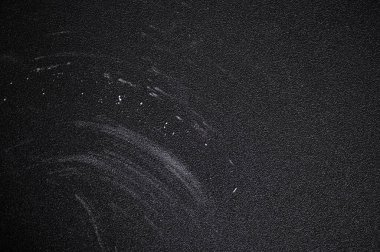 Beyaz toz, karmaşık kıvrımlı çizgiler ve dağınık noktalar yaratır. Karanlık, desenli bir arka plan boyunca çarpıcı bir kontrast sunar.