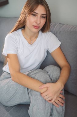 Genç bir kadın, gözleri kapalı bir kanepede oturuyor. Şakaklarını rahatsızlık içinde tutuyor. Çağdaş bir yaşam alanında baş ağrısı çektiğini gösteriyor..