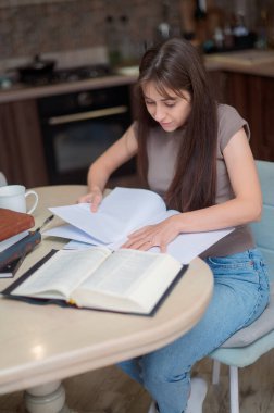 Bayan öğrenci çalışıyor ve evdeki sınava hazırlanıyor. Ders kitabını karıştıran ve notlar alan bir kadın.