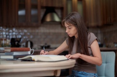 Bayan öğrenci çalışıyor ve evdeki sınava hazırlanıyor. Ders kitabını karıştıran ve notlar alan bir kadın.