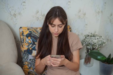 Kadın evinde rahat koltukta otururken cep telefonu kullanıyor, sosyal medyada geziniyor ya da arkadaşlarıyla sohbet ediyor.