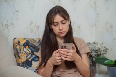 Kadın evinde rahat koltukta otururken cep telefonu kullanıyor, sosyal medyada geziniyor ya da arkadaşlarıyla sohbet ediyor.