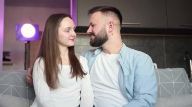 Romantik çift samimi bir anı paylaşıyor, kadın ve erkek modern dairelerinde bir kanepeye yaslanıyor, mor ortam aydınlatmasının yumuşak parıltısıyla banyo yapıyorlar.