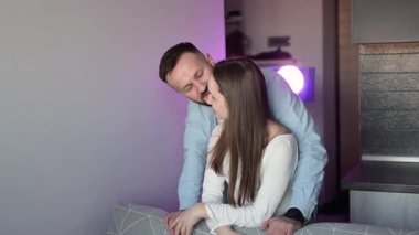 Romantik çift samimi bir anı paylaşıyor, kadın ve erkek modern dairelerinde bir kanepeye yaslanıyor, mor ortam aydınlatmasının yumuşak parıltısıyla banyo yapıyorlar.