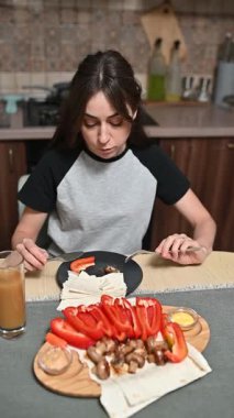 Mutfak masasında oturan genç bir kadın taze sebzeler, pide ekmeği ve besleyici sabah yemeği için meyve suyu hazırlıyor.