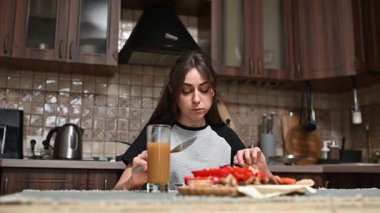 Mutfak masasında oturan genç bir kadın taze sebzeler, pide ekmeği ve besleyici sabah yemeği için meyve suyu hazırlıyor.