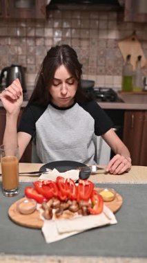 Mutfak masasında oturan genç bir kadın taze sebzeler, pide ekmeği ve besleyici sabah yemeği için meyve suyu hazırlıyor.