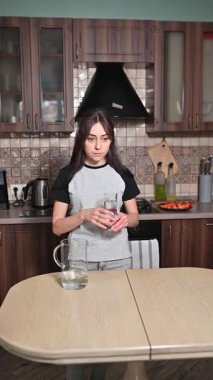 Genç bir kadın mutfakta bir bardak temiz su içiyor. Sağlıklı yaşam tarzı ve hidrasyon konsepti.